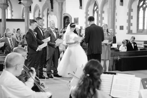 Black and white image of vicar, bride and groom with string quartet visible in foreground